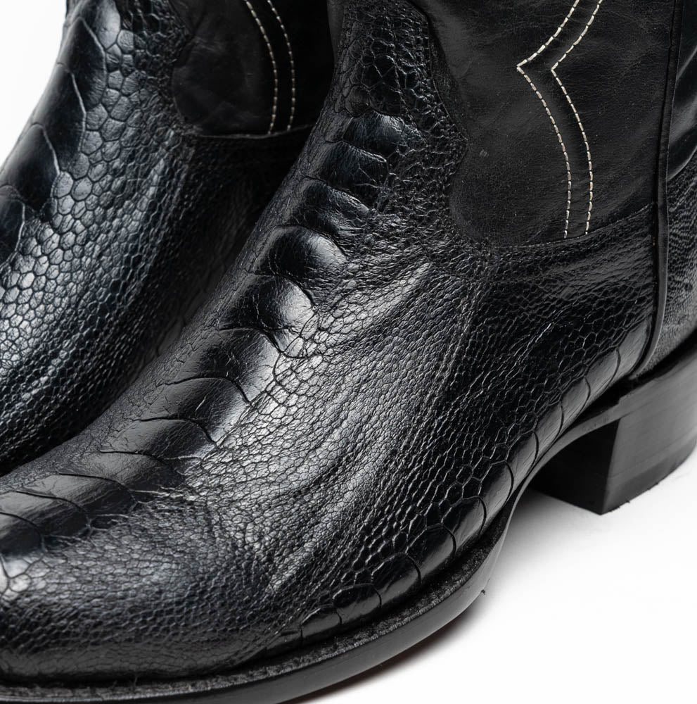 A pair of Denver Black cowboy boots by Marco Di Milano in genuine black ostrich leather, one upright and one displaying the sole with white stitching and the Marco Di Milano logo.