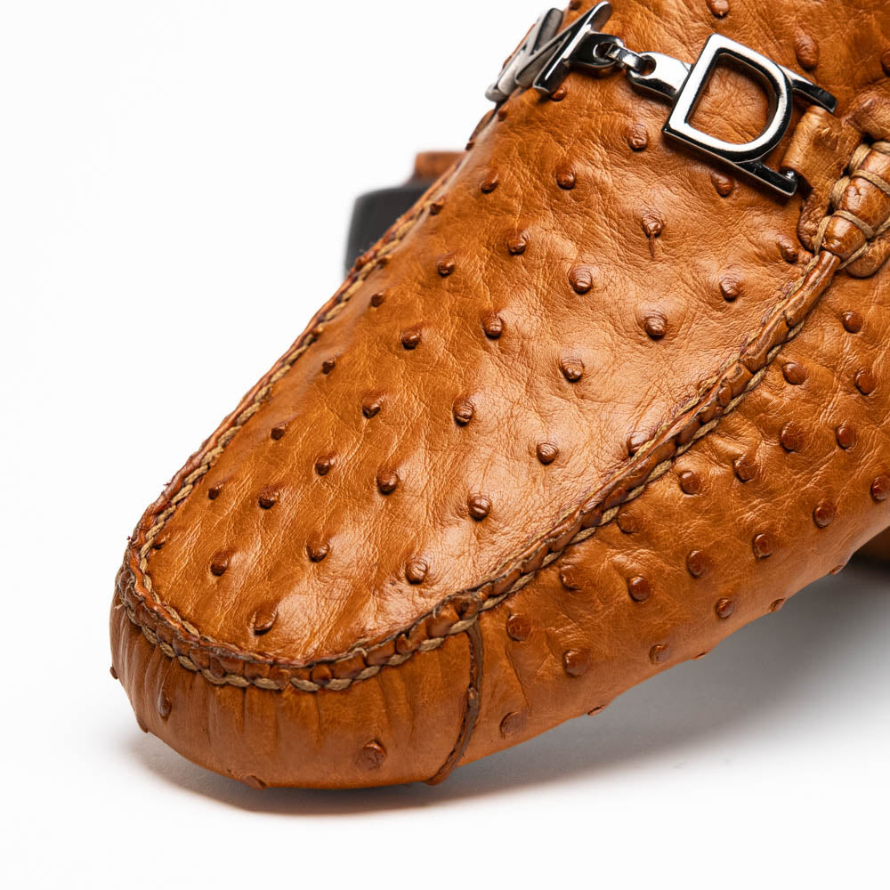 The Bolonia Brandy by Marco Di Milano—brown ostrich leather loafers with hand-painted finishes and metal buckles, one upright and one on its side revealing the sole—exude luxury, crafted from genuine exotic leather.