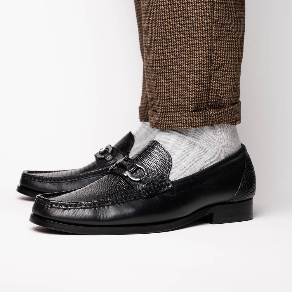 The Enzo Black by Marco Di Milano: black textured genuine lizard loafers with metal bit detail—one upright, one showing a brown sole stamped with "MARCO DI MILANO"—perfect for fans of luxury men's footwear.