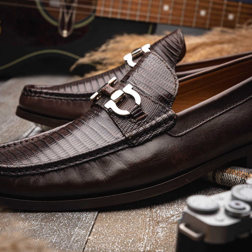 The Enzo Brown by Marco Di Milano features dark brown genuine lizard loafers with textured uppers, a metal buckle, and branded soles—luxurious men's footwear displayed against a white background.