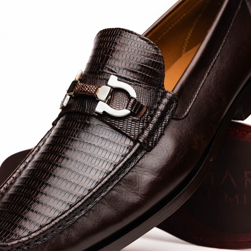 The Enzo Brown by Marco Di Milano features dark brown genuine lizard loafers with textured uppers, a metal buckle, and branded soles—luxurious men's footwear displayed against a white background.