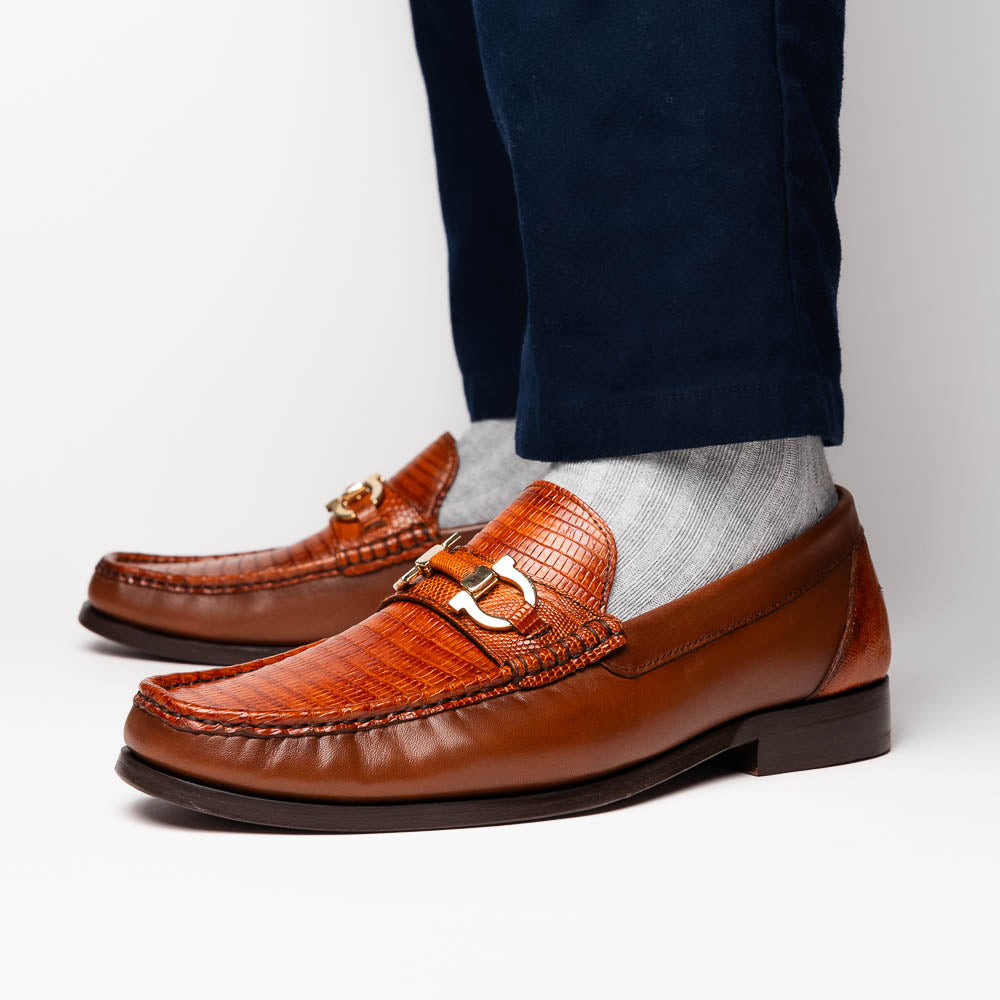 The Enzo Cognac by Marco Di Milano: men's brown leather loafers with a textured pattern, hand-painted finish, gold buckle, and black soles, shown on a white background.