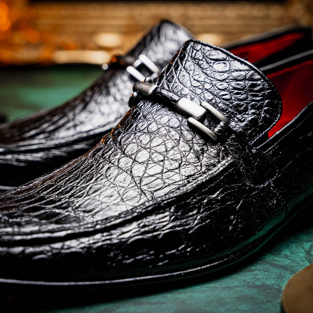 A pair of Fabro-Tin Black textured men's shoes by Marco Di Milano, featuring metal accents—one upright and one on its side showing the branded tan sole.