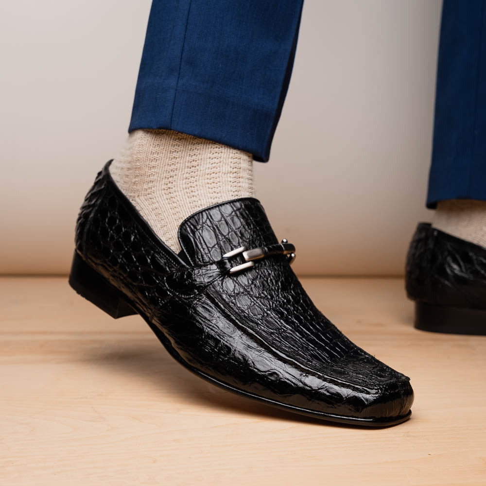 A pair of Fabro-Tin Black textured men's shoes by Marco Di Milano, featuring metal accents—one upright and one on its side showing the branded tan sole.