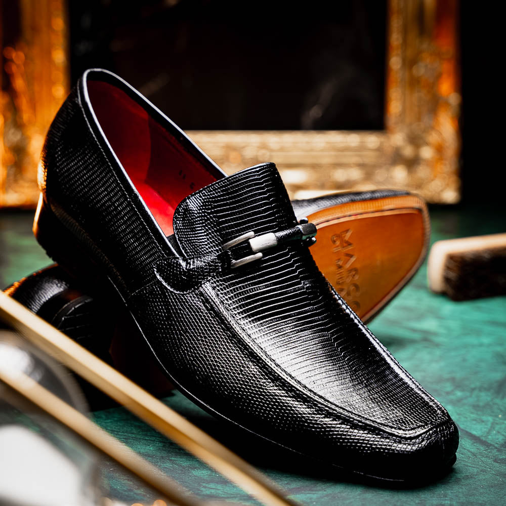 A pair of Marco Di Milano Fabro-Liz Black genuine lizard loafers, featuring textured leather, metal accents, and brown soles—one upright, the other on its side showing the luxury men's shoes branding on the sole.