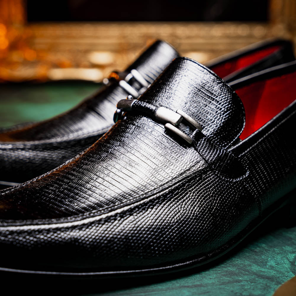 A pair of Marco Di Milano Fabro-Liz Black genuine lizard loafers, featuring textured leather, metal accents, and brown soles—one upright, the other on its side showing the luxury men's shoes branding on the sole.