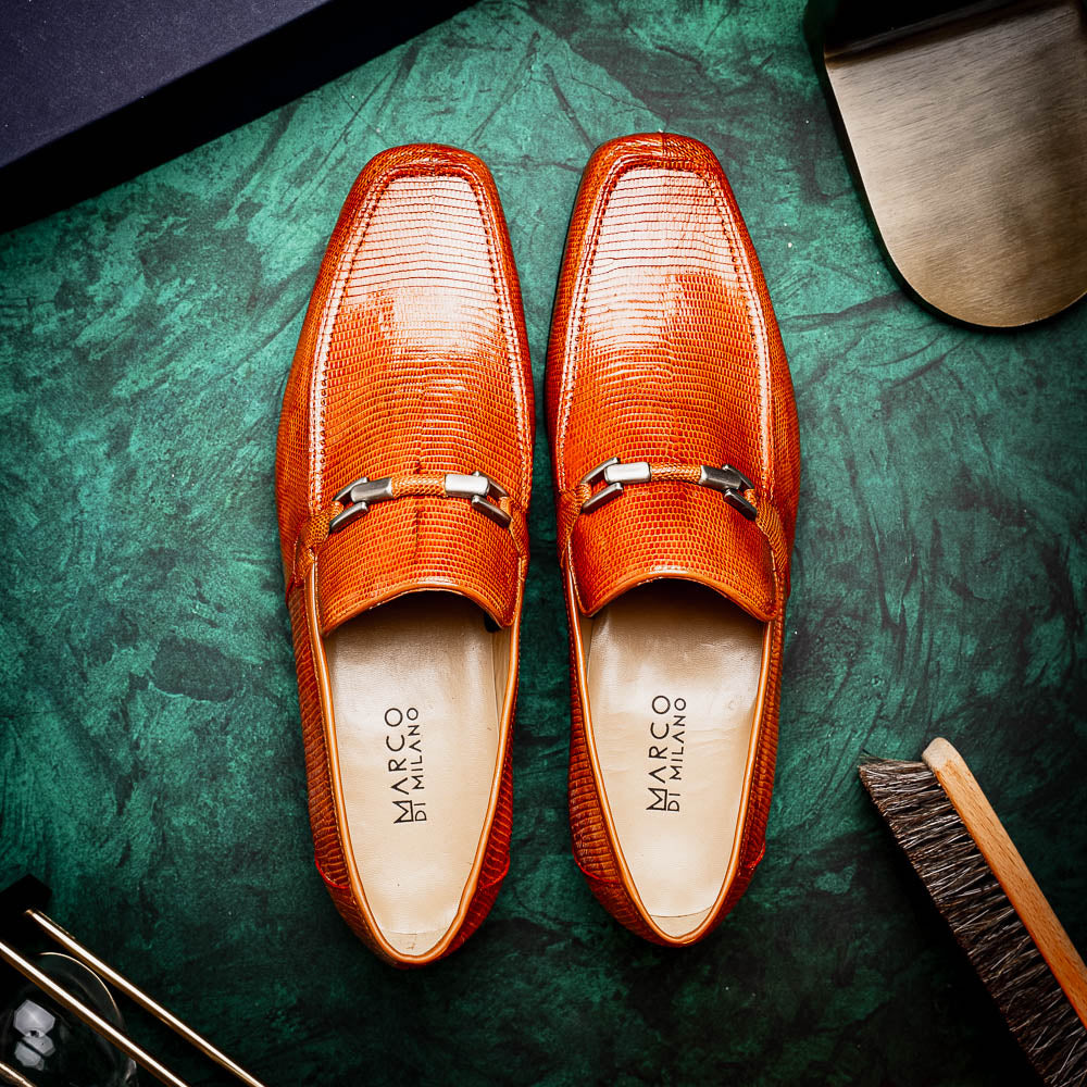 The Marco Di Milano Fabro-Liz Cognac loafers, crafted from brown leather with a textured finish and metal detail, are displayed—one upright and one showing the sole and branding—showcasing refined luxury footwear.