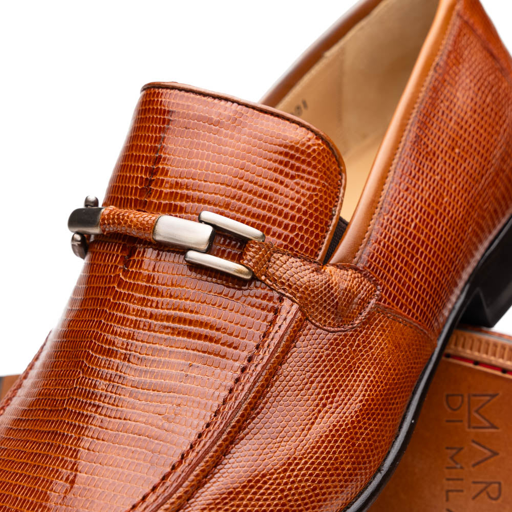 The Marco Di Milano Fabro-Liz Cognac loafers, crafted from brown leather with a textured finish and metal detail, are displayed—one upright and one showing the sole and branding—showcasing refined luxury footwear.