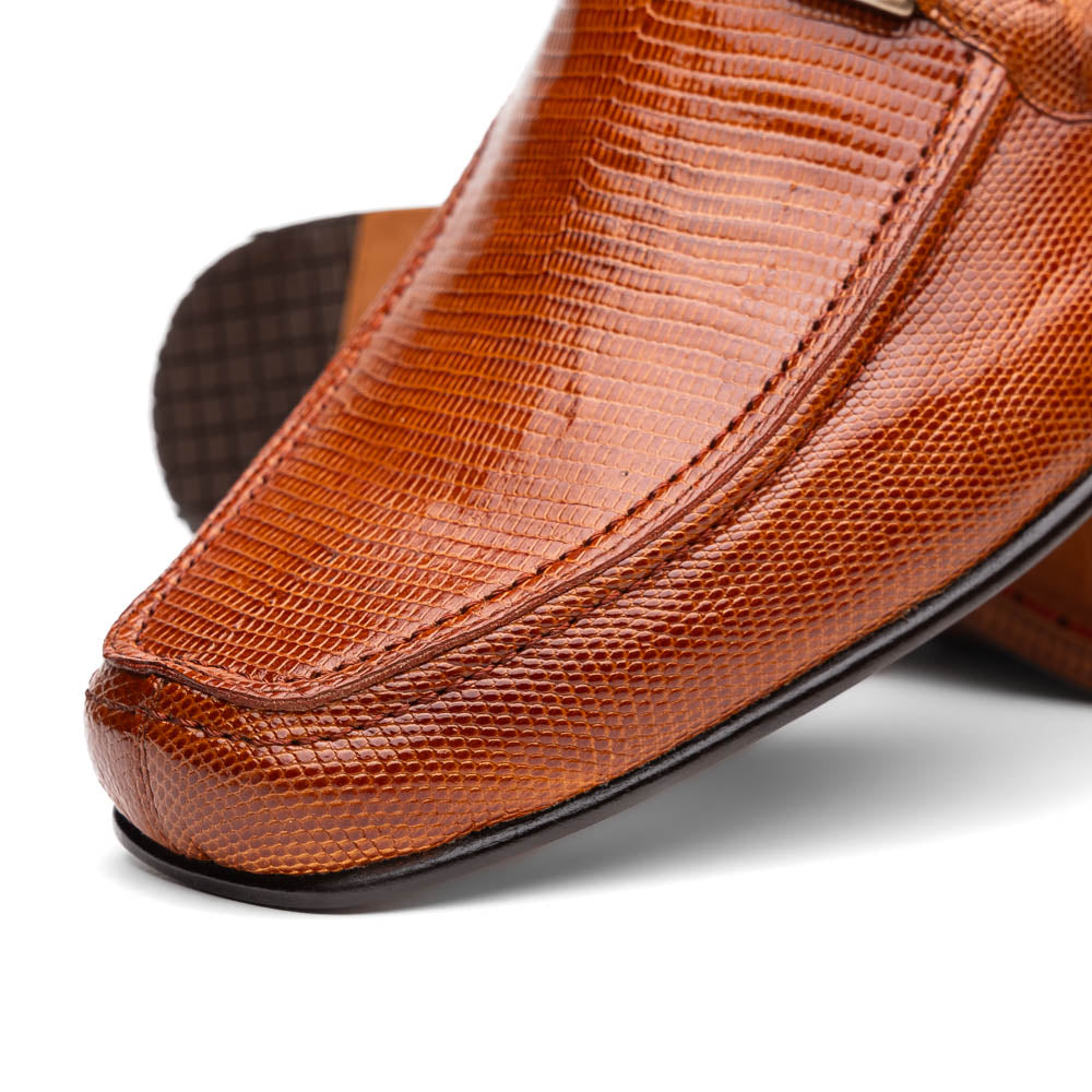 The Marco Di Milano Fabro-Liz Cognac loafers, crafted from brown leather with a textured finish and metal detail, are displayed—one upright and one showing the sole and branding—showcasing refined luxury footwear.