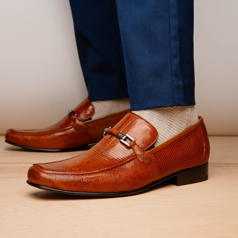 The Marco Di Milano Fabro-Liz Cognac loafers, crafted from brown leather with a textured finish and metal detail, are displayed—one upright and one showing the sole and branding—showcasing refined luxury footwear.