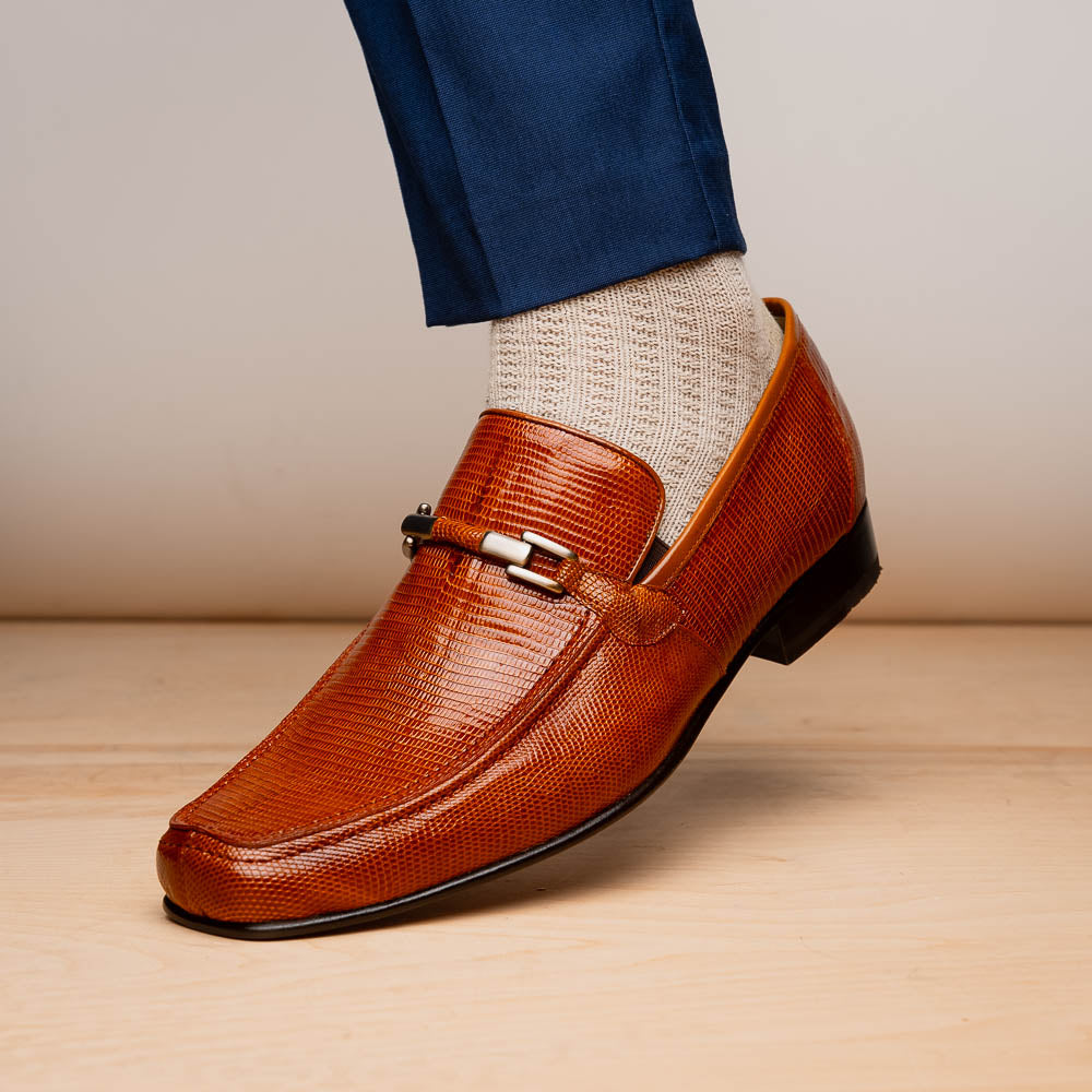 The Marco Di Milano Fabro-Liz Cognac loafers, crafted from brown leather with a textured finish and metal detail, are displayed—one upright and one showing the sole and branding—showcasing refined luxury footwear.