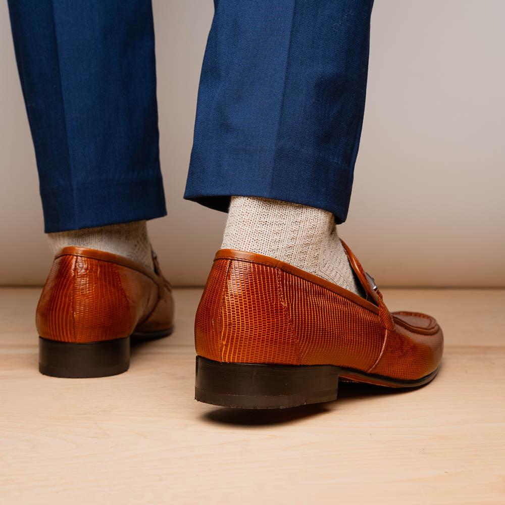 The Marco Di Milano Fabro-Liz Cognac loafers, crafted from brown leather with a textured finish and metal detail, are displayed—one upright and one showing the sole and branding—showcasing refined luxury footwear.
