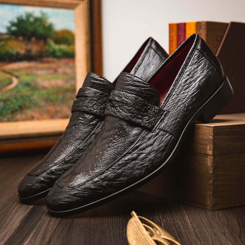 The Fangio Black by Marco Di Milano: a pair of black textured leather loafers, one upright and one sole-up, displaying the brand on the tan sole—luxury men's footwear to elevate any look.
