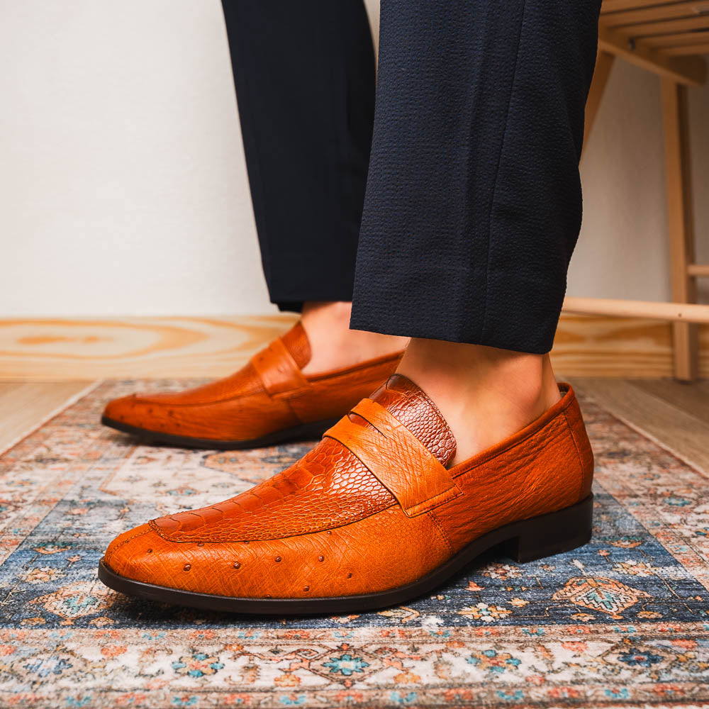 A pair of Marco Di Milano Fangio Cognac men's shoes in brown leather with textured detailing; one genuine ostrich loafer stands upright, while the other lies on its side showing the sole embossed with the brand name.