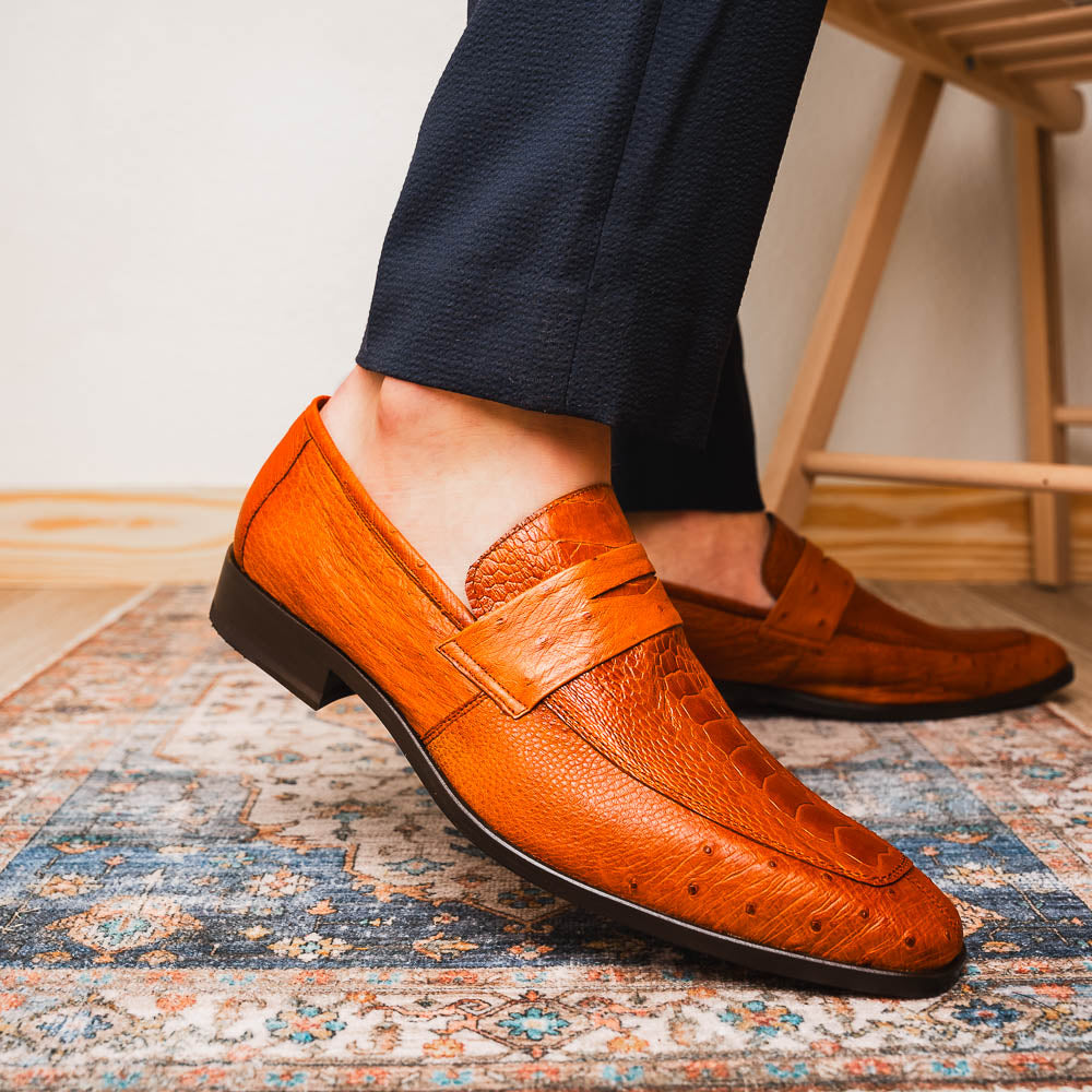 A pair of Marco Di Milano Fangio Cognac men's shoes in brown leather with textured detailing; one genuine ostrich loafer stands upright, while the other lies on its side showing the sole embossed with the brand name.