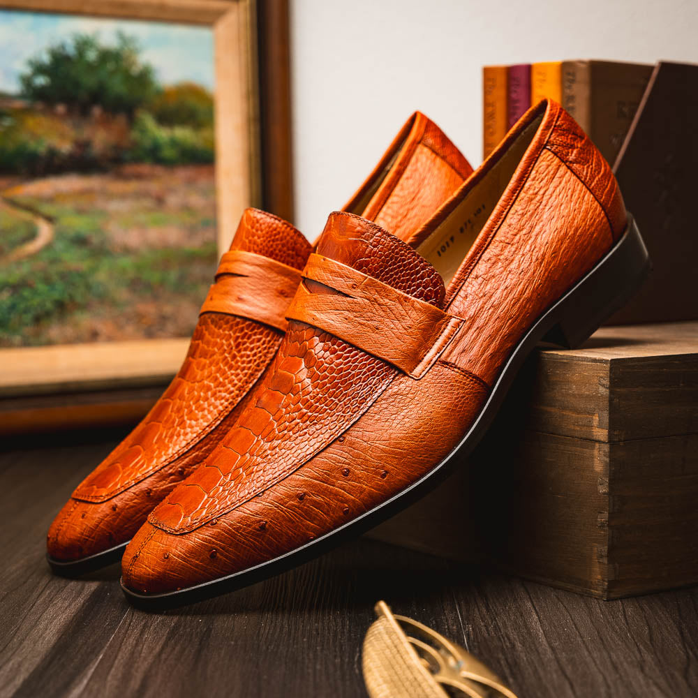 A pair of Marco Di Milano Fangio Cognac men's shoes in brown leather with textured detailing; one genuine ostrich loafer stands upright, while the other lies on its side showing the sole embossed with the brand name.