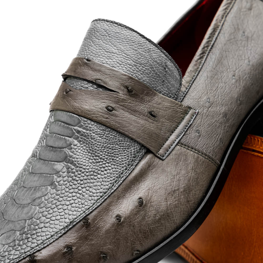 The Fangio Serpentine Gray by Marco Di Milano features gray textured leather in classic penny loafer style, with detailed stitching and tan leather soles—one shoe upright, one on its side—to showcase refined craftsmanship.