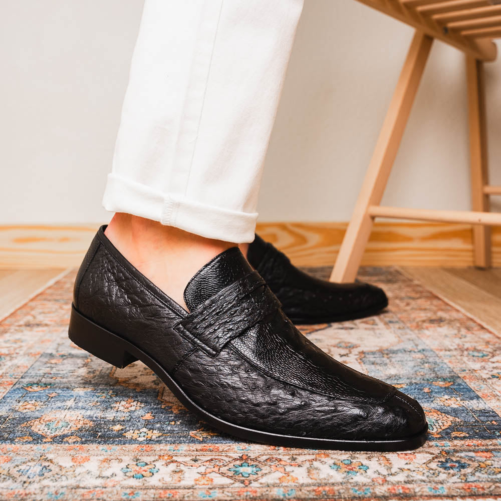 The Fangio Black by Marco Di Milano: a pair of black textured leather loafers, one upright and one sole-up, displaying the brand on the tan sole—luxury men's footwear to elevate any look.