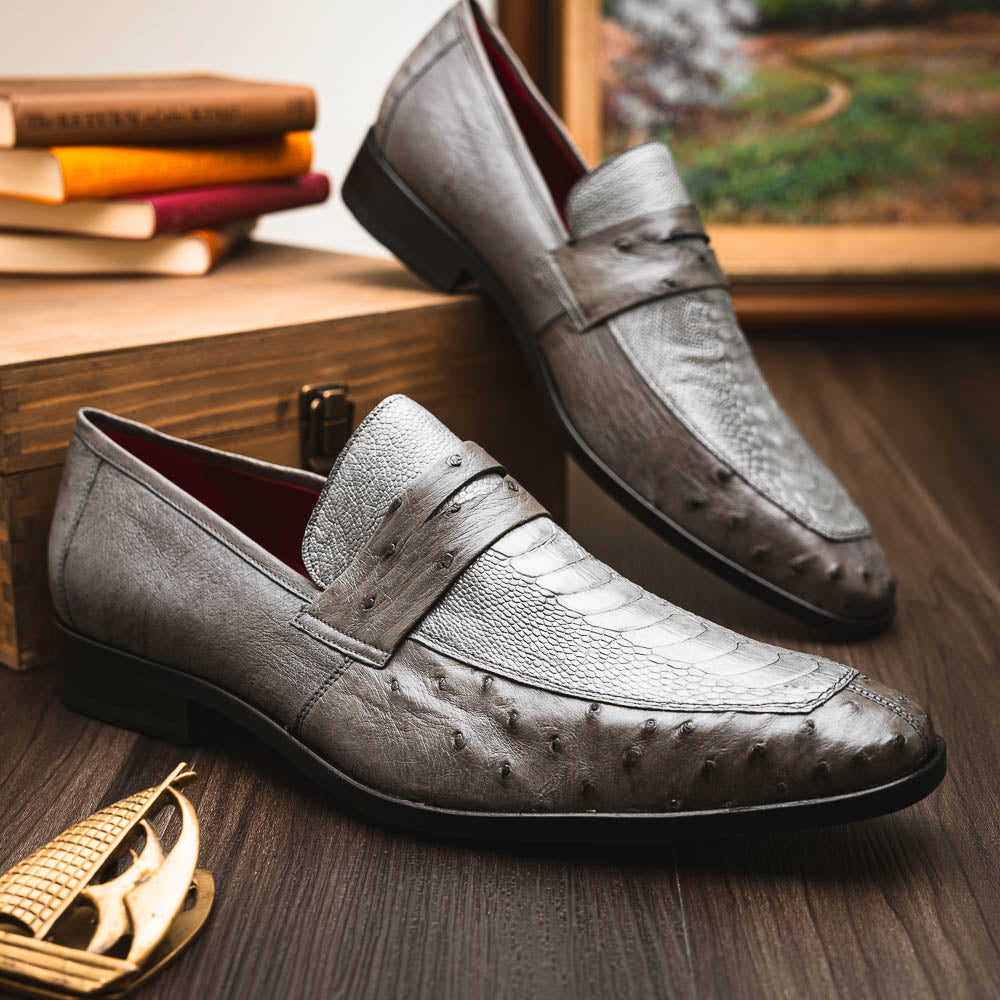 The Fangio Serpentine Gray by Marco Di Milano features gray textured leather in classic penny loafer style, with detailed stitching and tan leather soles—one shoe upright, one on its side—to showcase refined craftsmanship.
