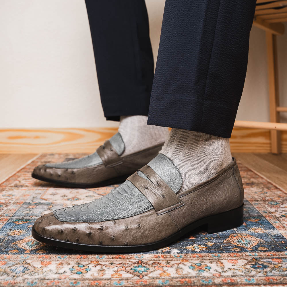 The Fangio Serpentine Gray by Marco Di Milano features gray textured leather in classic penny loafer style, with detailed stitching and tan leather soles—one shoe upright, one on its side—to showcase refined craftsmanship.
