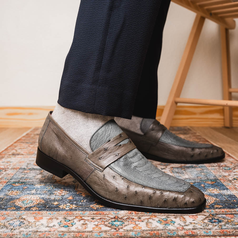 The Fangio Serpentine Gray by Marco Di Milano features gray textured leather in classic penny loafer style, with detailed stitching and tan leather soles—one shoe upright, one on its side—to showcase refined craftsmanship.
