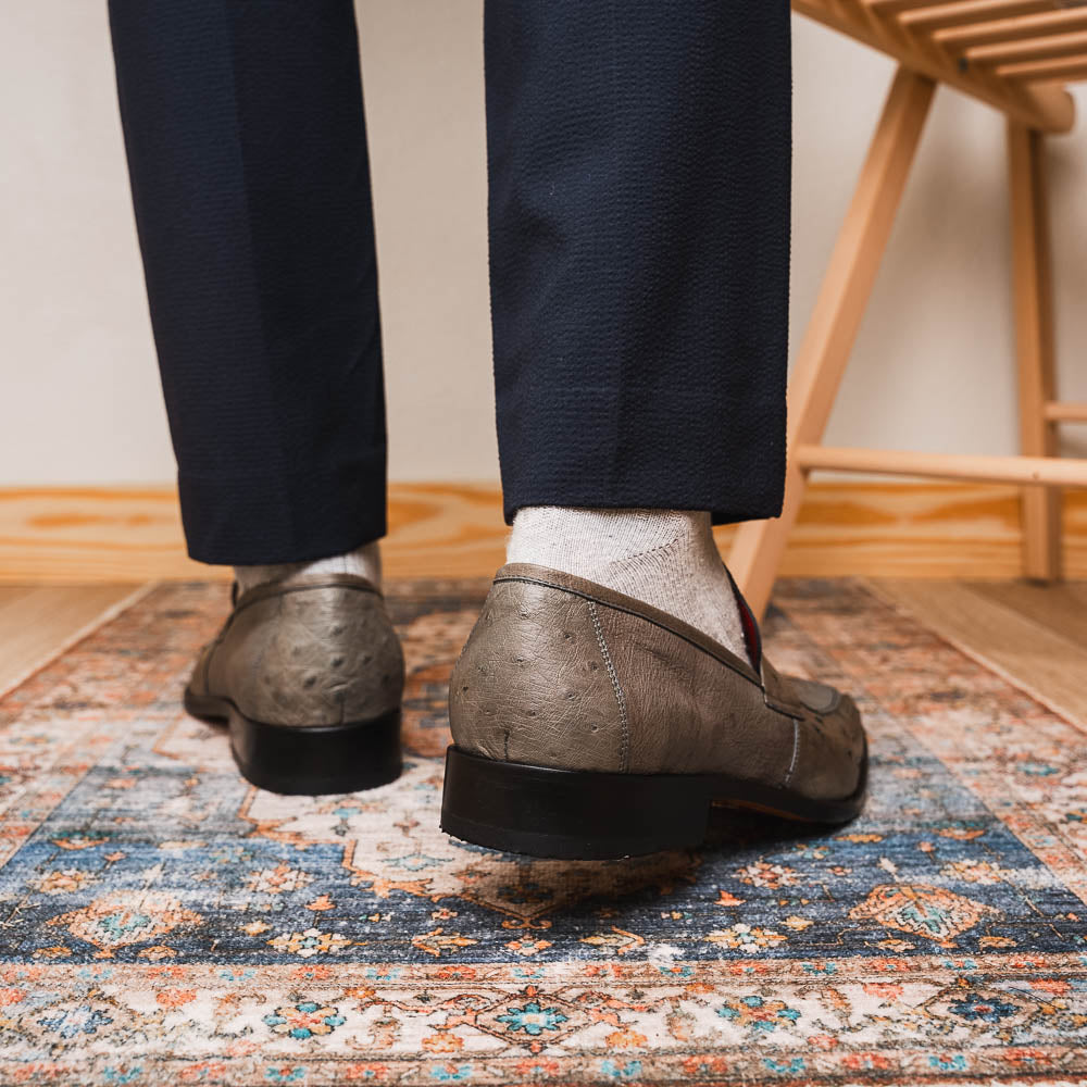 The Fangio Serpentine Gray by Marco Di Milano features gray textured leather in classic penny loafer style, with detailed stitching and tan leather soles—one shoe upright, one on its side—to showcase refined craftsmanship.