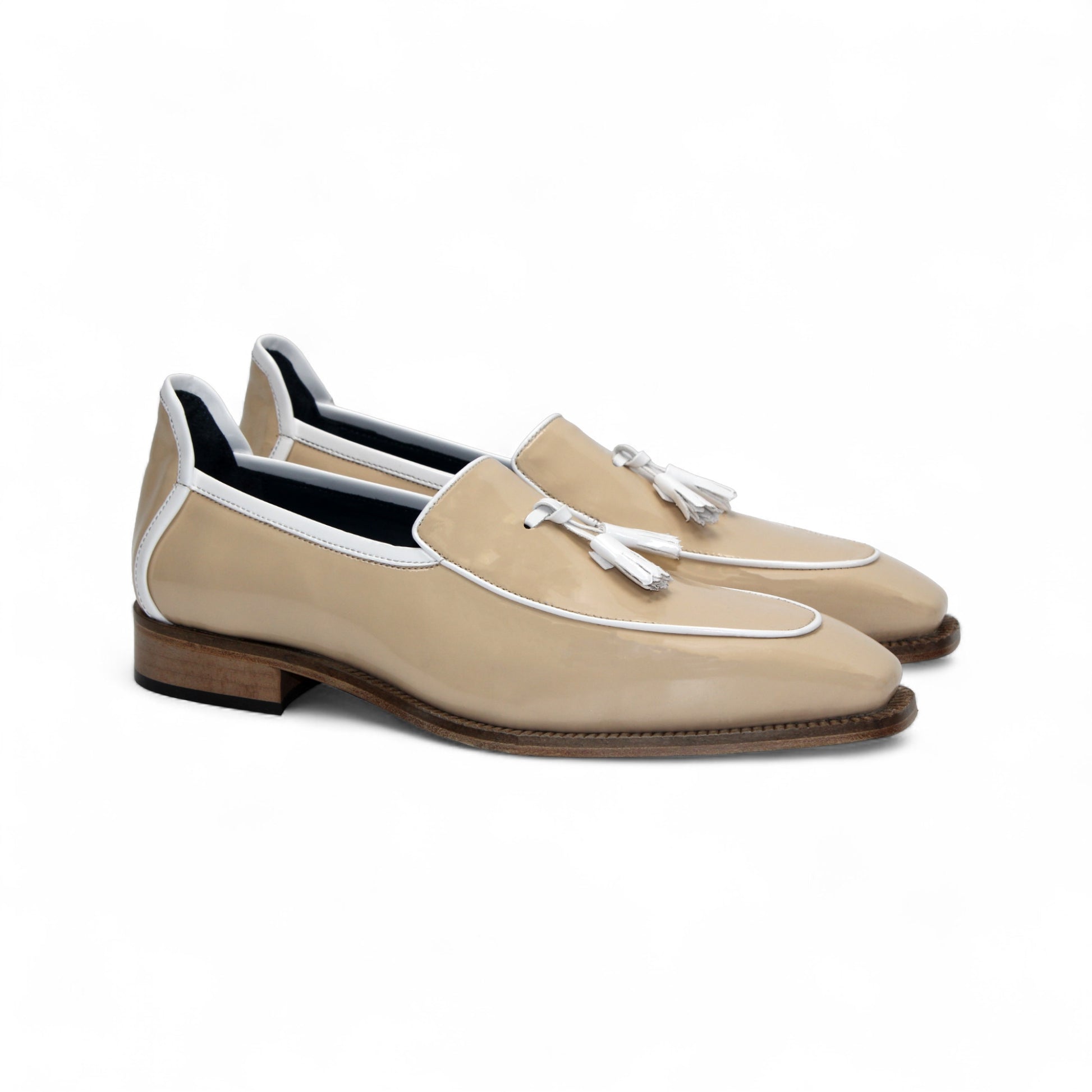 The Duca Di Matiste Duca Fano Cream/White loafer features beige patent leather, white trim, a wooden heel, and decorative tassels. This minimalist, elegant shoe is beautifully crafted in Italy. Shown in profile view.