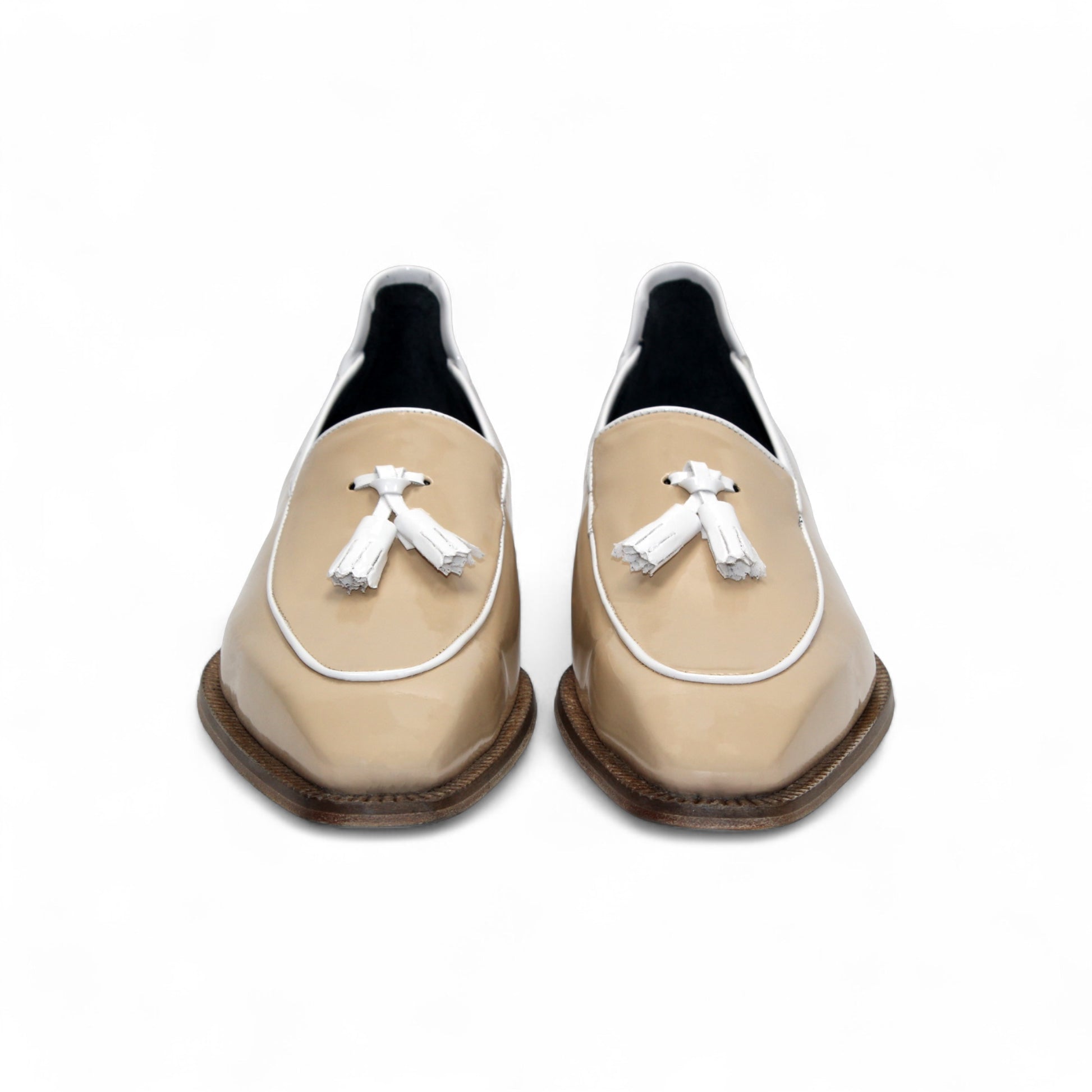 The Duca Di Matiste Duca Fano Cream/White loafer features beige patent leather, white trim, a wooden heel, and decorative tassels. This minimalist, elegant shoe is beautifully crafted in Italy. Shown in profile view.