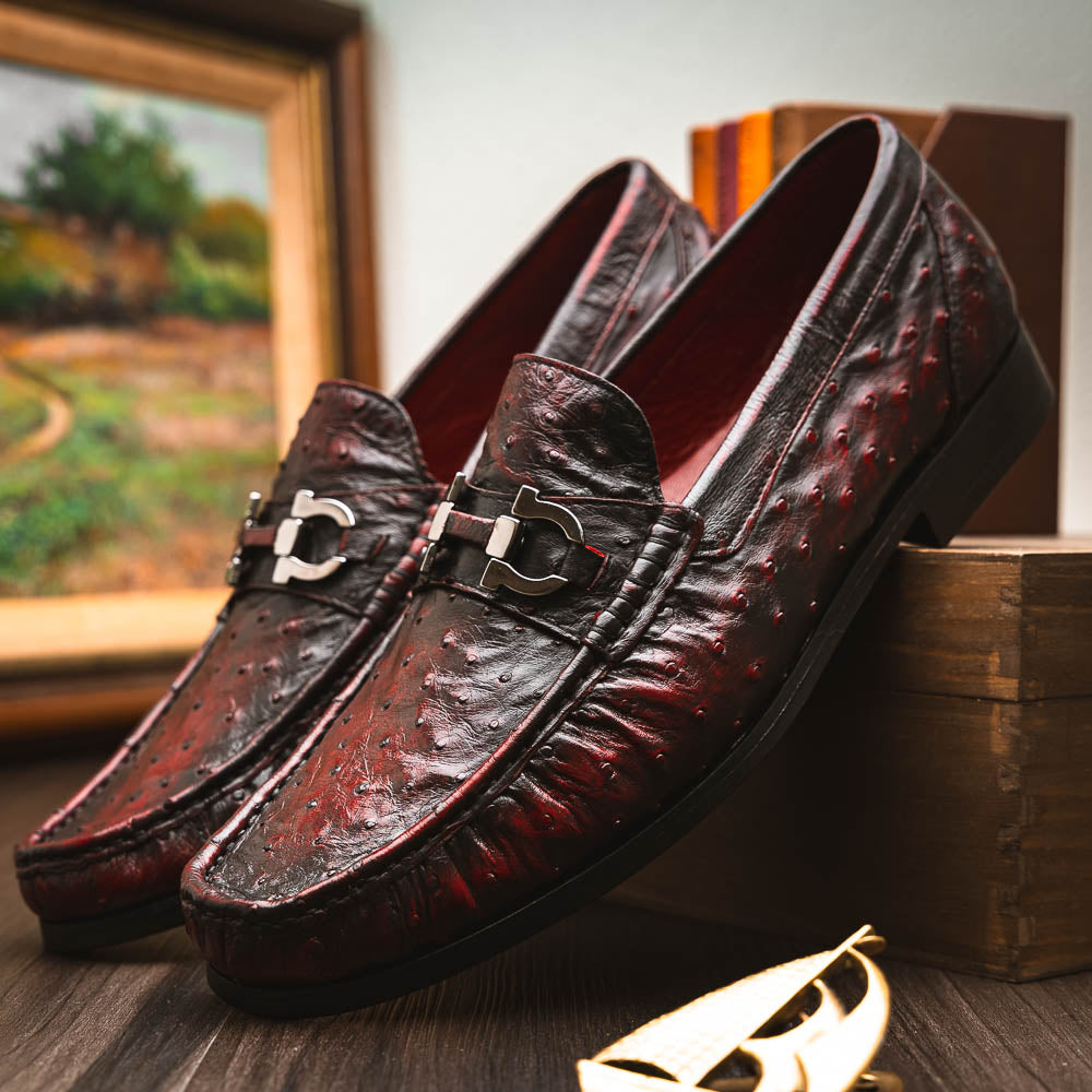 The Marco Di Milano Ferrioni BlackCherry loafers, shown with one upright and one on its side to reveal the sole, feature classic metal bit detailing—ideal for those seeking luxury men's footwear.