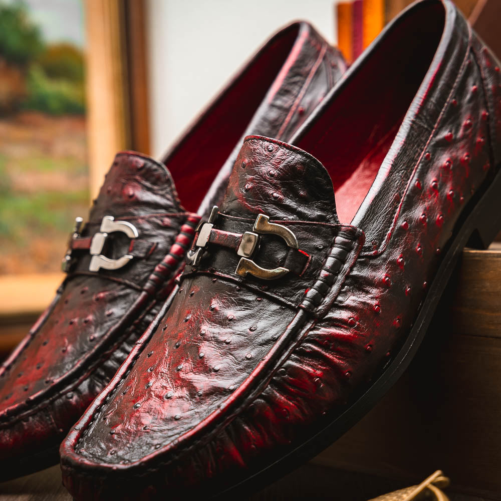 The Marco Di Milano Ferrioni BlackCherry loafers, shown with one upright and one on its side to reveal the sole, feature classic metal bit detailing—ideal for those seeking luxury men's footwear.