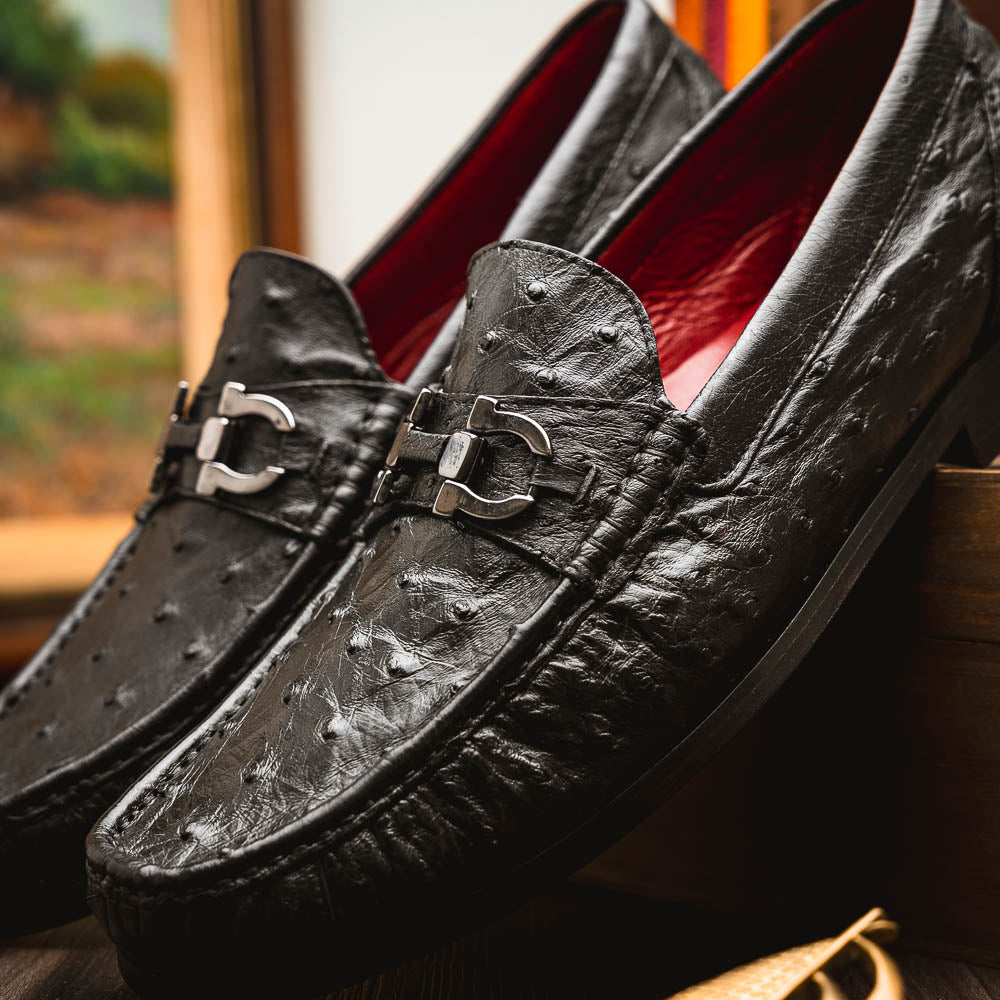 The Marco Di Milano Ferrioni Black: luxury men's loafers in genuine ostrich leather with metal buckles and brown soles, shown both upright and on their side to highlight the branding.