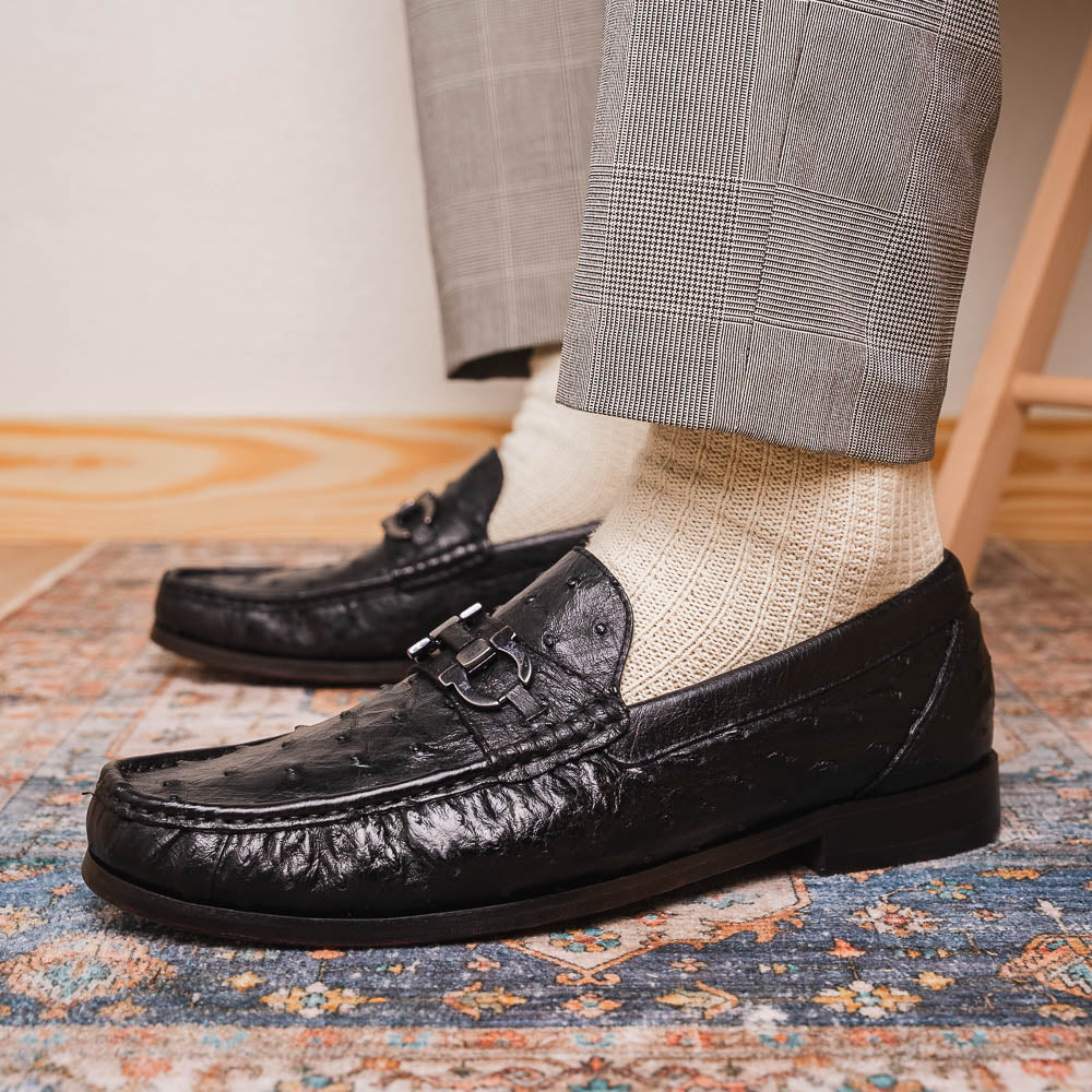 The Marco Di Milano Ferrioni Black: luxury men's loafers in genuine ostrich leather with metal buckles and brown soles, shown both upright and on their side to highlight the branding.