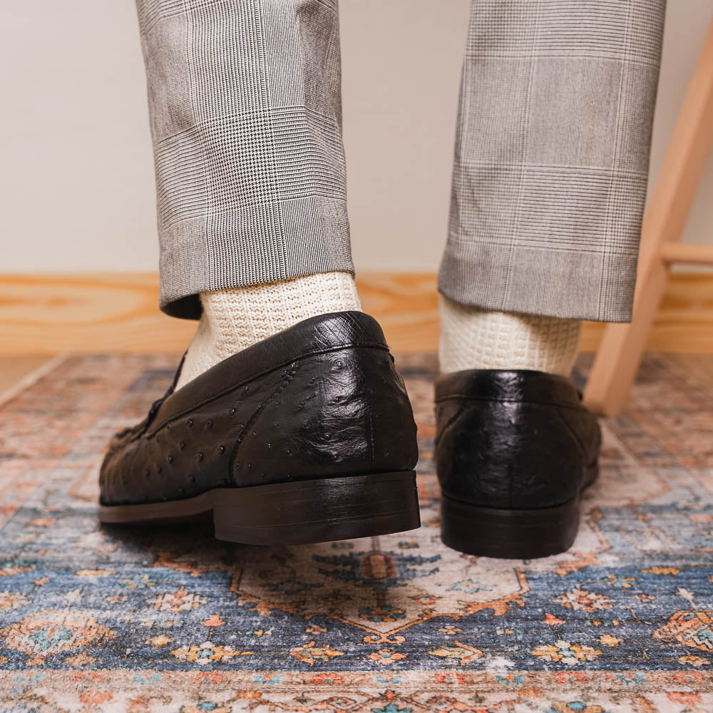 The Marco Di Milano Ferrioni Black: luxury men's loafers in genuine ostrich leather with metal buckles and brown soles, shown both upright and on their side to highlight the branding.