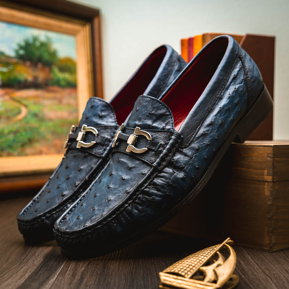 A pair of luxury men's shoes: Ferrioni Navy loafers by Marco Di Milano in genuine ostrich leather, featuring classic bit detail. One shoe is upright, the other shows the sole with "Marco Di Milano" branding.