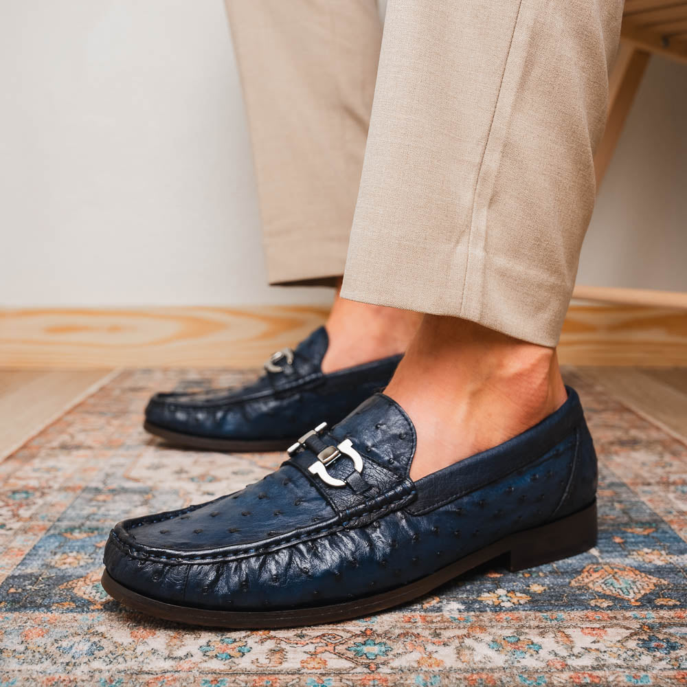 A pair of luxury men's shoes: Ferrioni Navy loafers by Marco Di Milano in genuine ostrich leather, featuring classic bit detail. One shoe is upright, the other shows the sole with "Marco Di Milano" branding.