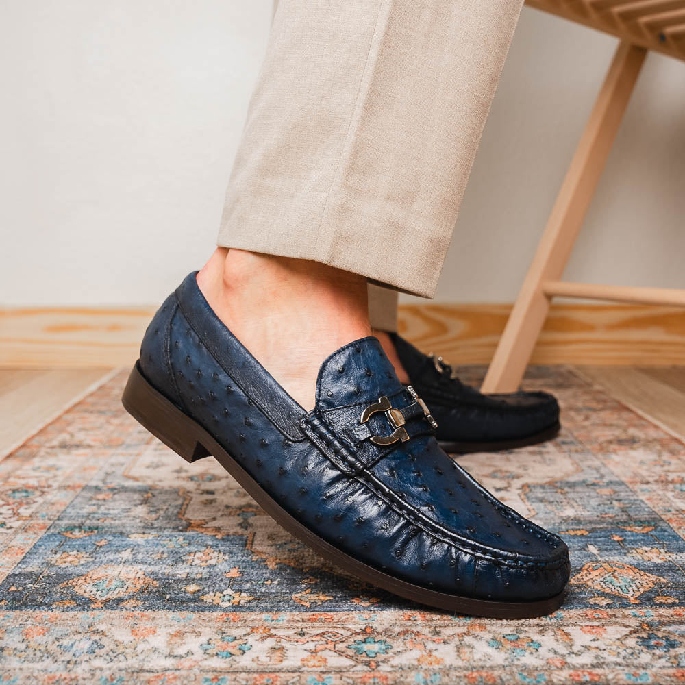 A pair of luxury men's shoes: Ferrioni Navy loafers by Marco Di Milano in genuine ostrich leather, featuring classic bit detail. One shoe is upright, the other shows the sole with "Marco Di Milano" branding.