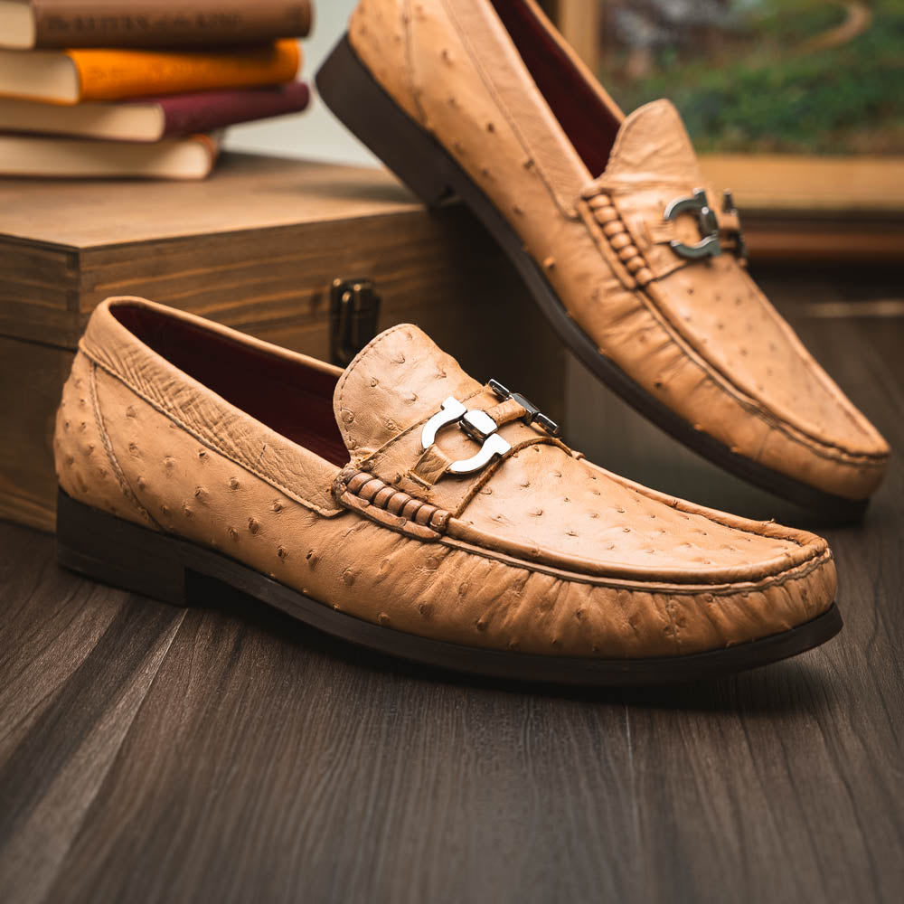 The Marco Di Milano Ferrioni Orix is a pair of genuine beige ostrich loafers with a classic bit buckle, one upright and one on its side showing the insole logo—timeless luxury men's footwear.