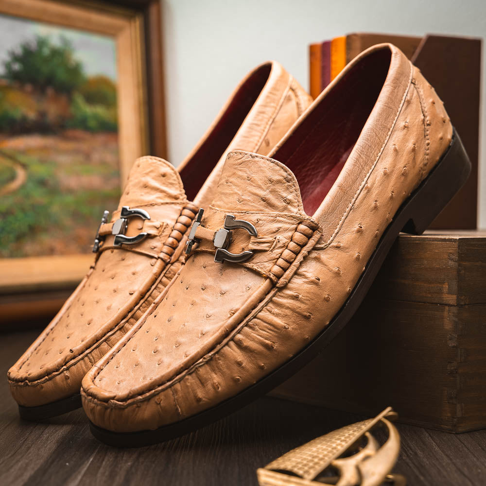 The Marco Di Milano Ferrioni Orix is a pair of genuine beige ostrich loafers with a classic bit buckle, one upright and one on its side showing the insole logo—timeless luxury men's footwear.