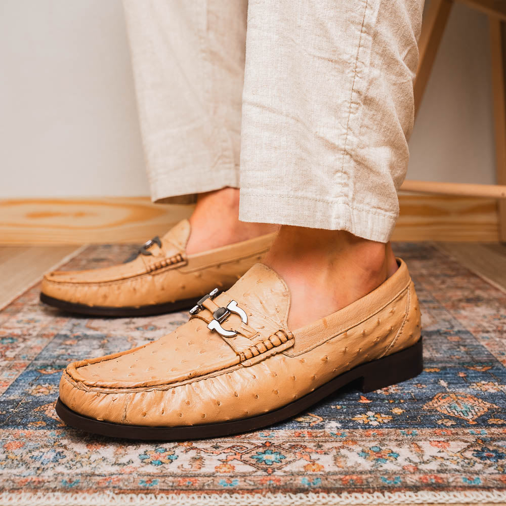 The Marco Di Milano Ferrioni Orix is a pair of genuine beige ostrich loafers with a classic bit buckle, one upright and one on its side showing the insole logo—timeless luxury men's footwear.