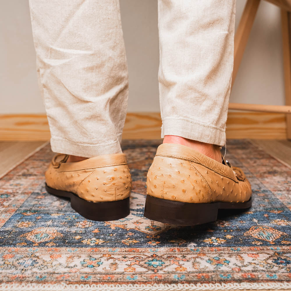 The Marco Di Milano Ferrioni Orix is a pair of genuine beige ostrich loafers with a classic bit buckle, one upright and one on its side showing the insole logo—timeless luxury men's footwear.