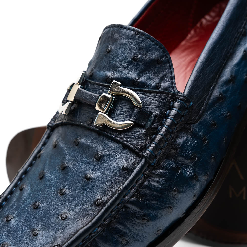 A pair of luxury men's shoes: Ferrioni Navy loafers by Marco Di Milano in genuine ostrich leather, featuring classic bit detail. One shoe is upright, the other shows the sole with "Marco Di Milano" branding.