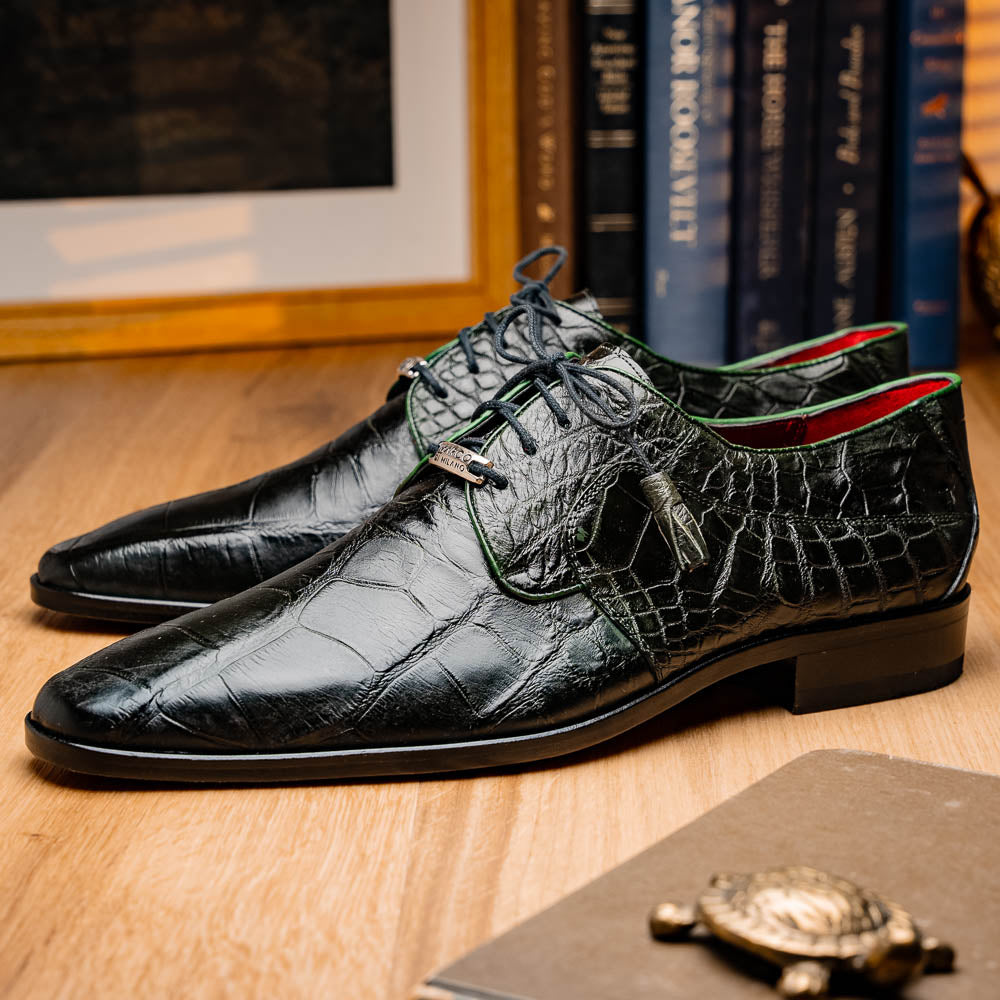 A pair of Fitipaldi Olive luxury footwear by Marco Di Milano in black crocodile leather—one shoe upright, the other showing a tan sole with "Marco Di Milano" embossed—crafted with hand-painted finishes for an elegant touch.