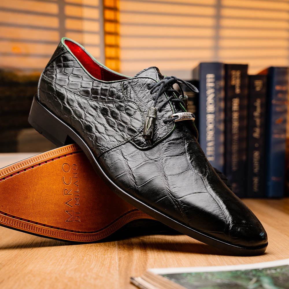 A pair of Fitipaldi Olive luxury footwear by Marco Di Milano in black crocodile leather—one shoe upright, the other showing a tan sole with "Marco Di Milano" embossed—crafted with hand-painted finishes for an elegant touch.