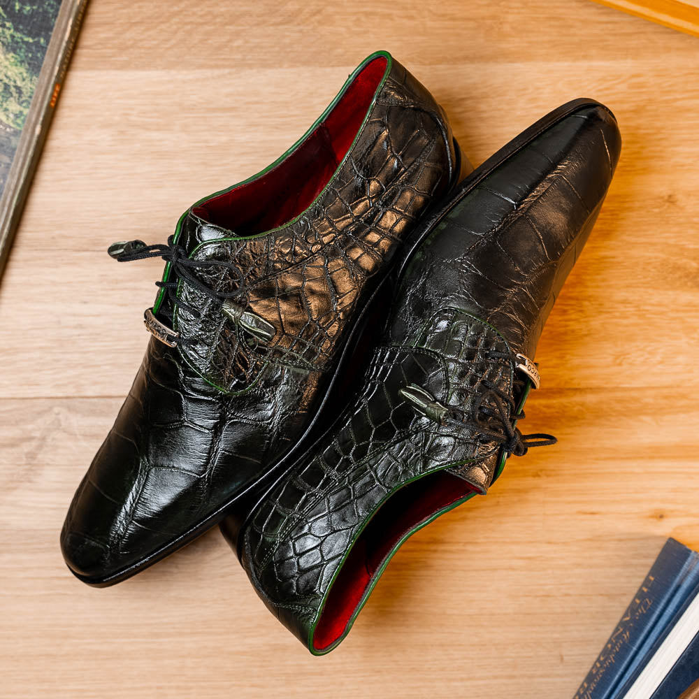A pair of Fitipaldi Olive luxury footwear by Marco Di Milano in black crocodile leather—one shoe upright, the other showing a tan sole with "Marco Di Milano" embossed—crafted with hand-painted finishes for an elegant touch.