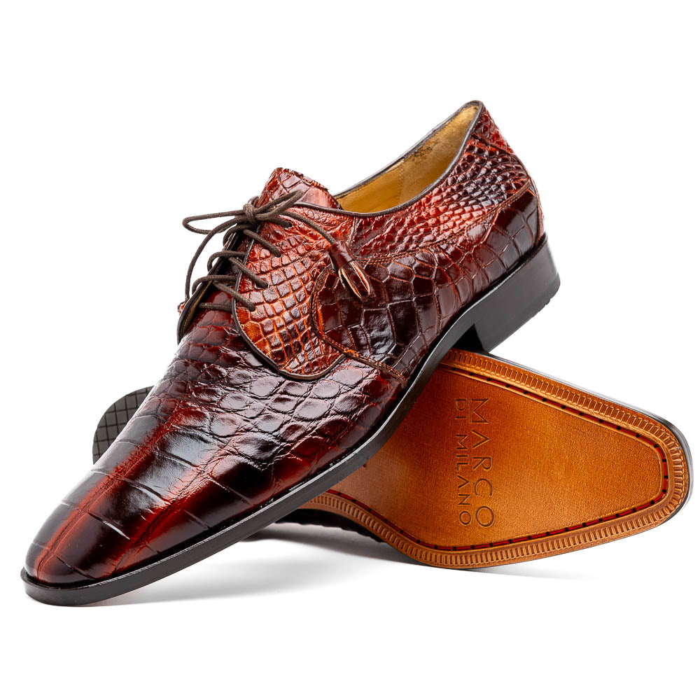 A pair of Fitipaldi Rustic Cognac shoes by Marco Di Milano in brown crocodile-patterned leather—one upright, one displaying the sole with branding—showcases exquisite hand-painted finishes, epitomizing luxury footwear.