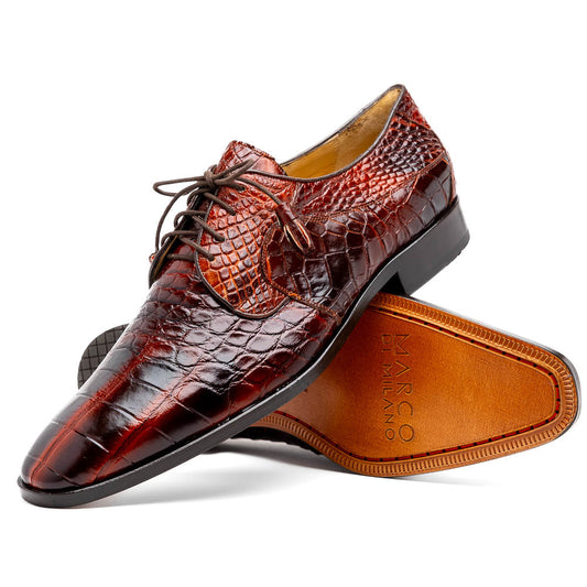 A pair of Fitipaldi Rustic Cognac shoes by Marco Di Milano in brown crocodile-patterned leather—one upright, one displaying the sole with branding—showcases exquisite hand-painted finishes, epitomizing luxury footwear.