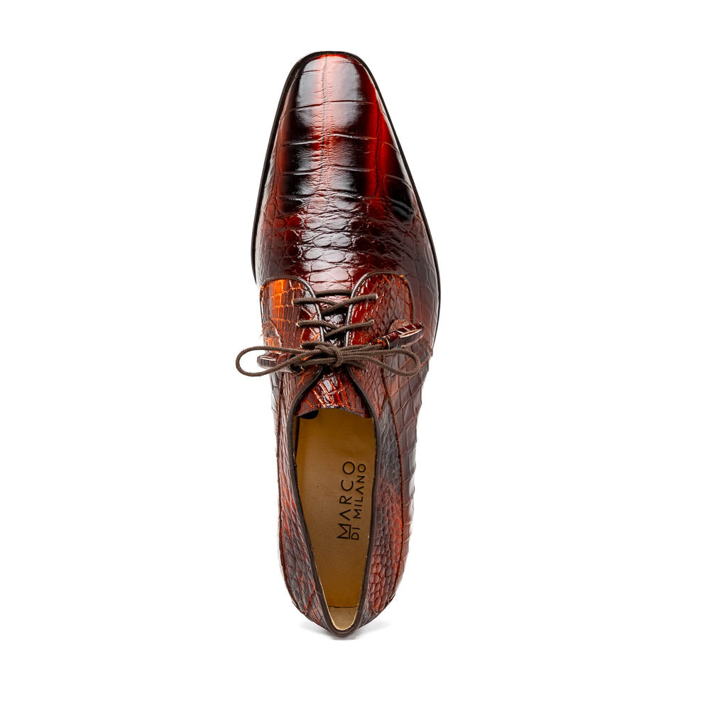 A pair of Fitipaldi Rustic Cognac shoes by Marco Di Milano in brown crocodile-patterned leather—one upright, one displaying the sole with branding—showcases exquisite hand-painted finishes, epitomizing luxury footwear.