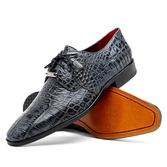 A pair of gray crocodile-pattern luxury dress shoes, the Fitipaldi Rustic Gray by Marco Di Milano, are shown—one upright and one on its side—to display a tan sole marked "Marco Di Milano." Hand-painted finishes showcase exquisite craftsmanship.