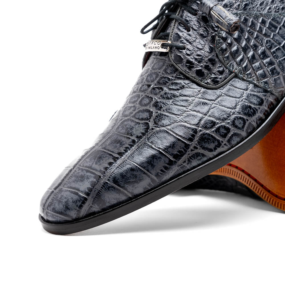 A pair of gray crocodile-pattern luxury dress shoes, the Fitipaldi Rustic Gray by Marco Di Milano, are shown—one upright and one on its side—to display a tan sole marked "Marco Di Milano." Hand-painted finishes showcase exquisite craftsmanship.