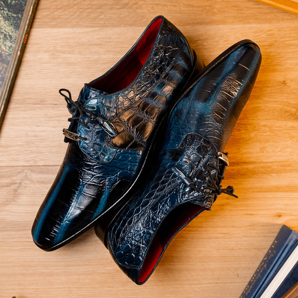 Fitipaldi Rustic Navy by Marco Di Milano: a pair of blue leather men’s dress shoes with a crocodile pattern, black soles, and lace-up fronts; one luxury shoe is shown on its side to display the tan sole.